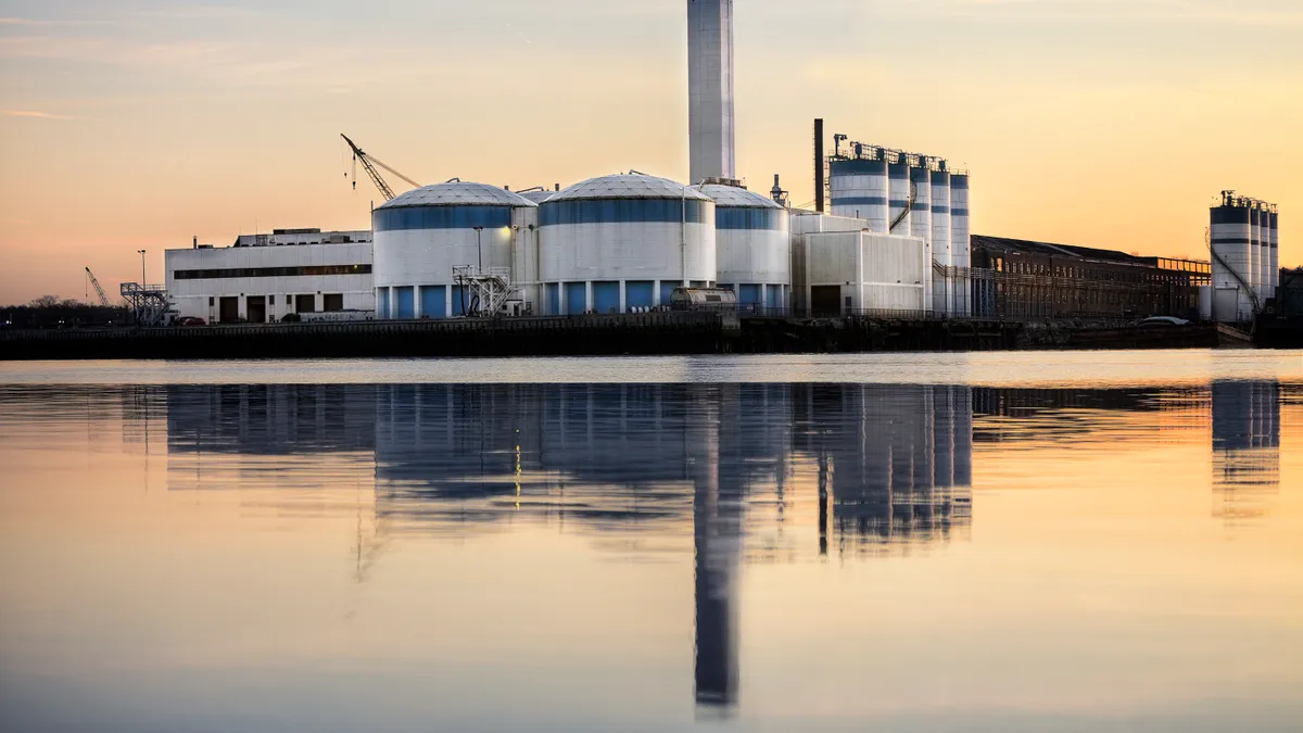 An industrial facility with several large tanks sits along a waterfront.