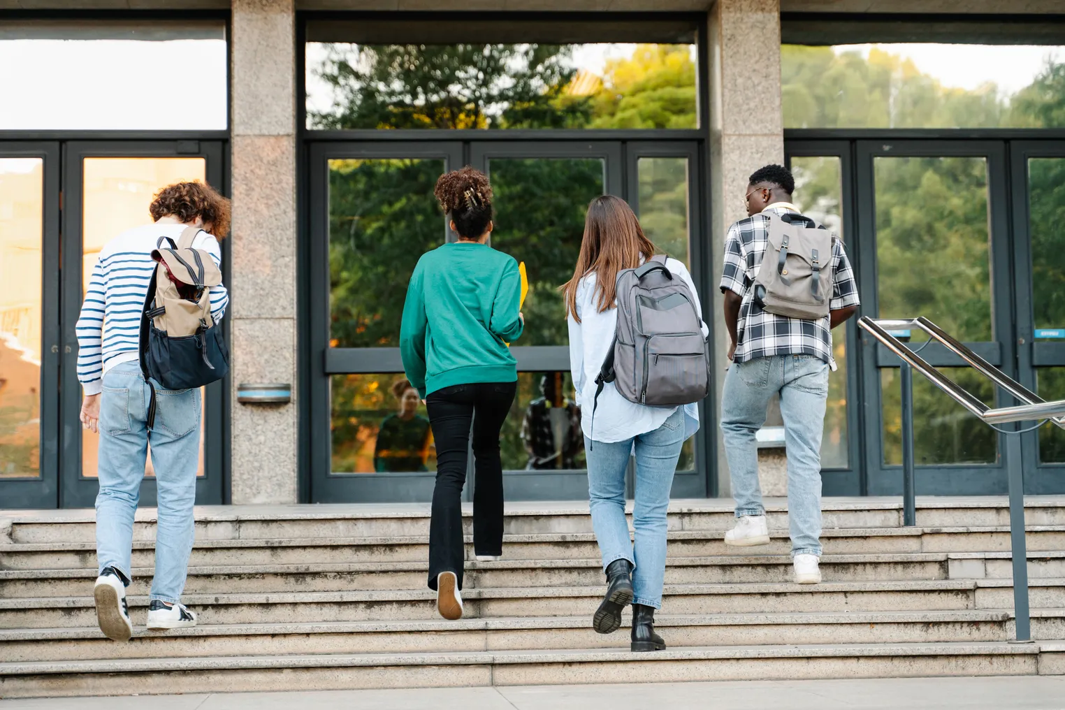 Four college students walk up the steps to a building entrance.