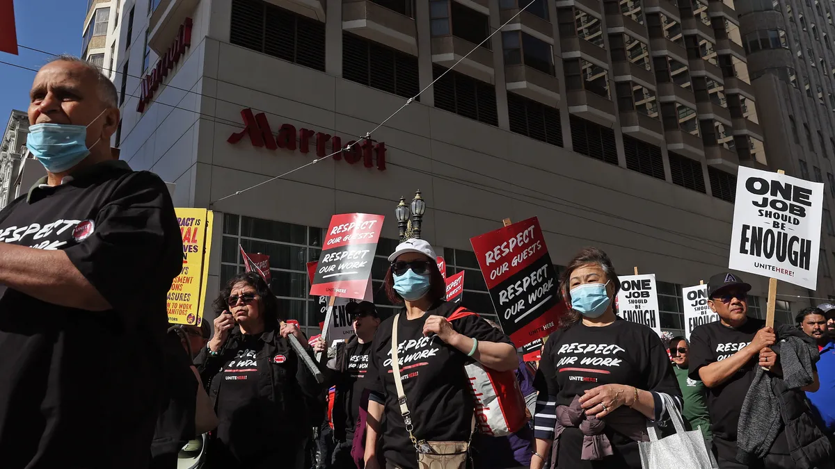 Workers march holding signs reading "One Job Is Enough."