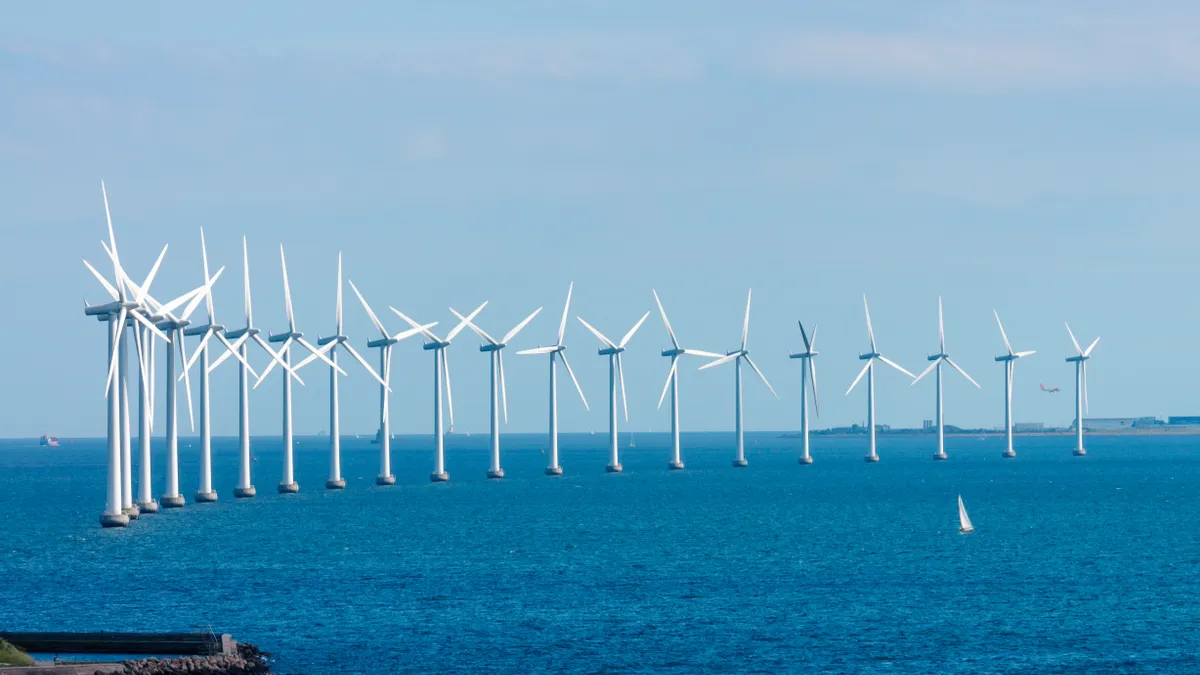 Offshore wind turbines stand in a semicircle in the ocean.