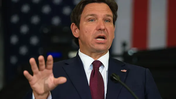 A close-up shot of Gov. Ron DeSantis speaking at a podium with an American flag as the backdrop.