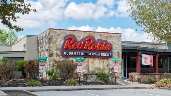 A daytime photograph of a building with a stone facade and a large red sign that says "Red Robin." The parking lot in front of the building is empty.