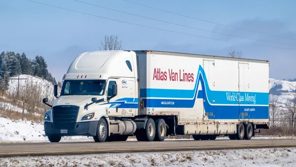 A white Atlas Van Lines semi-truck with blue and red accents travels on a snowy road in Calgary, Alberta.