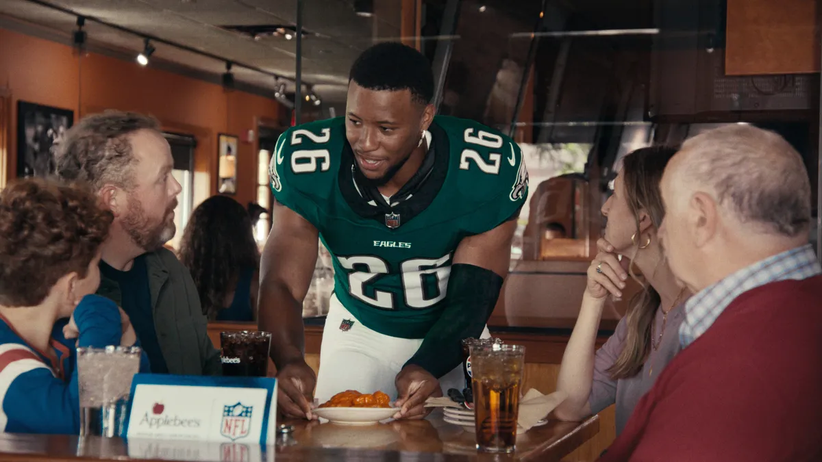 NFL player Saquon Barkley serves food at an Applebee's