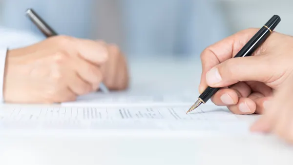 A picture of two hands holding pens signing a document.