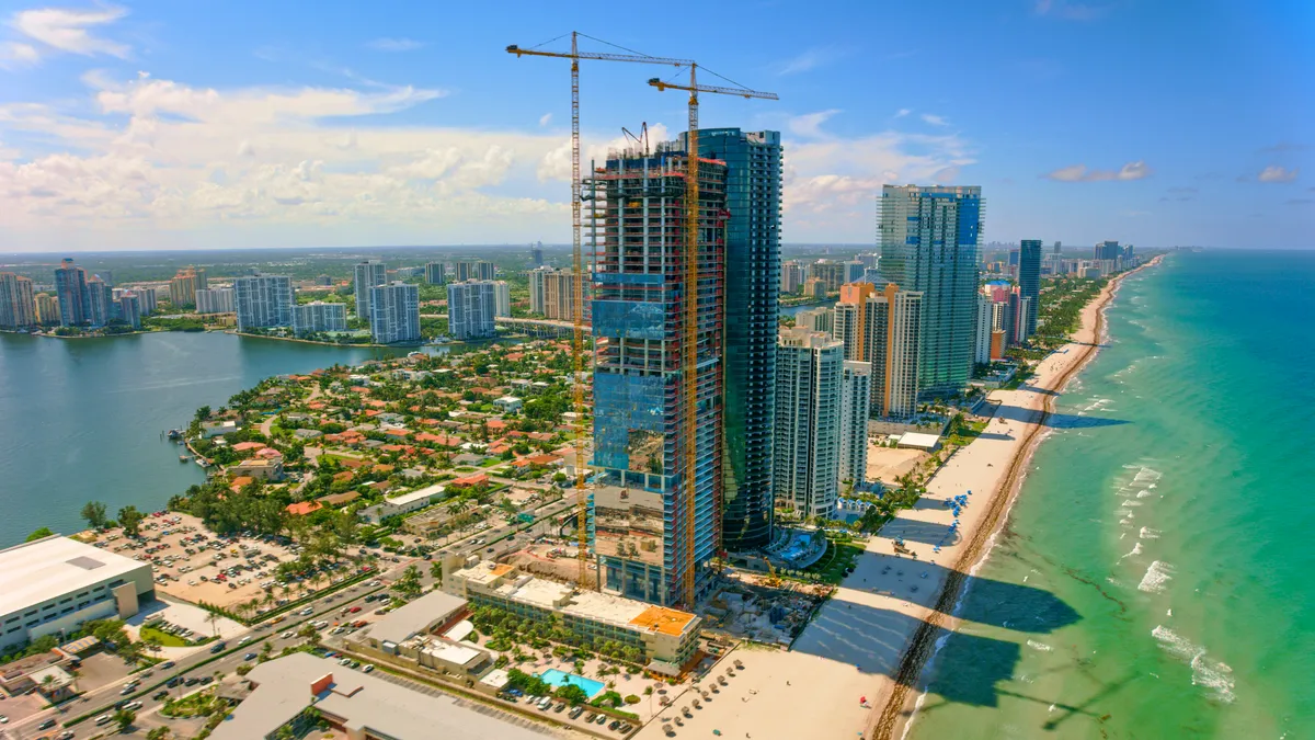 A crane hovers above a hotel tower along the beach.