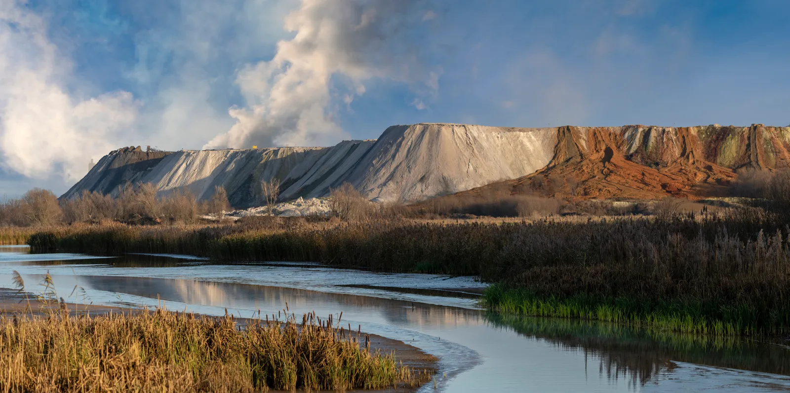 Huge phosphogypsum heaps on the banks of contaminated sewage sludge with a smoky blue sky in the background.