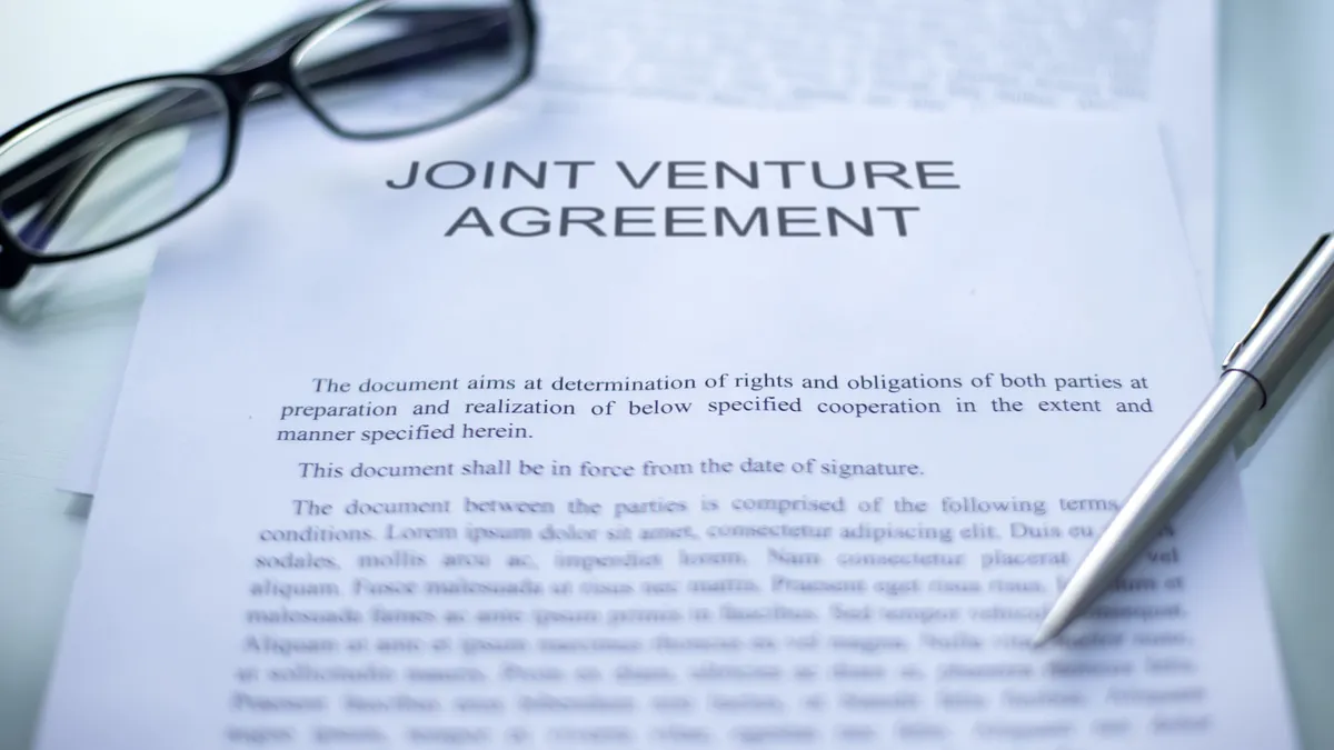 Joint venture agreement, pen and eyeglasses lying on table.