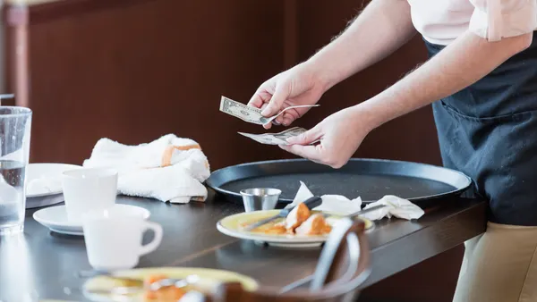 A waiter picks up a cash tip from a table.