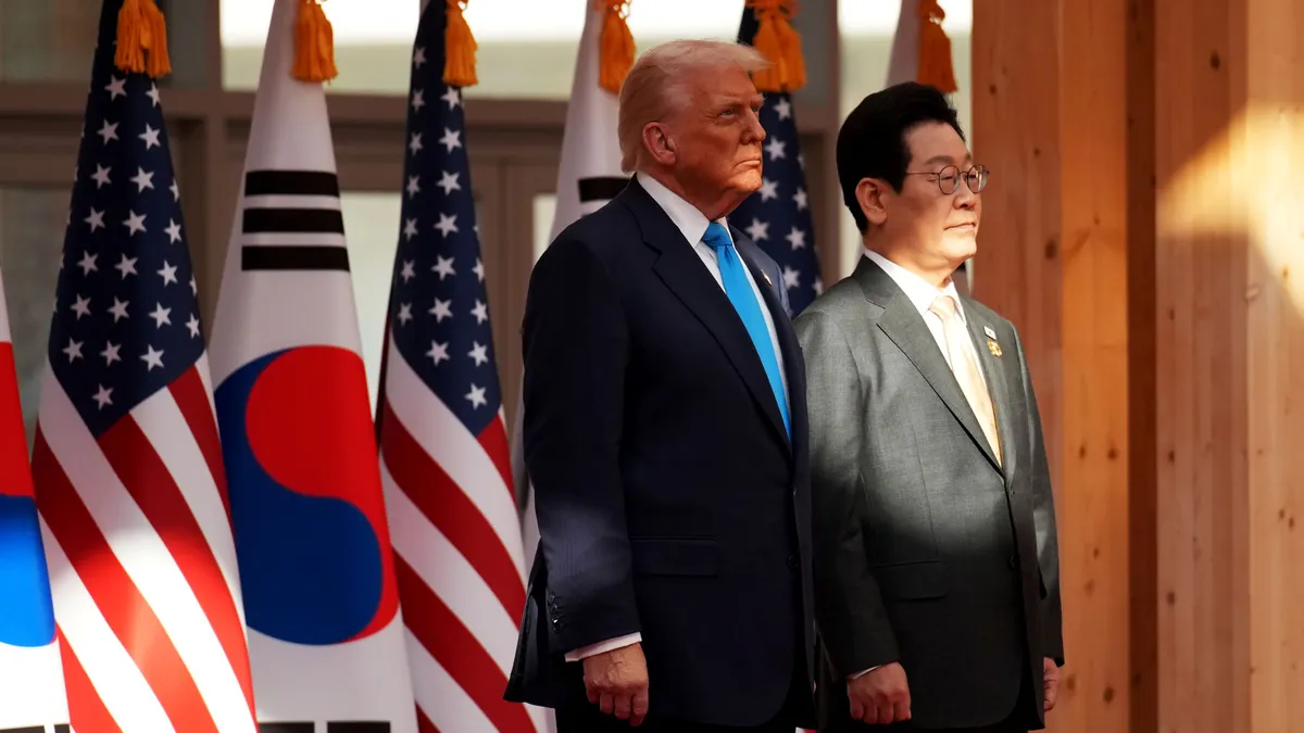 U.S. President Donald Trump stands next to South Korea President Lee Jae Myung in front of several flags from both countries.