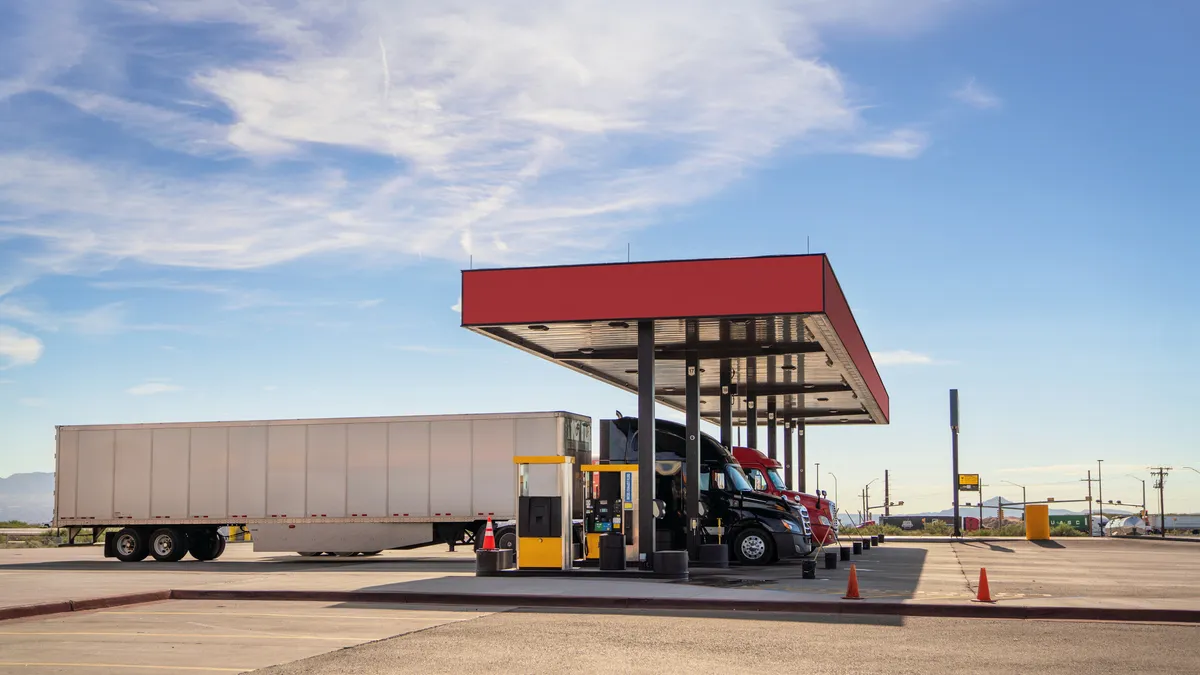 Semi trucks refueling at a station in Texas with blue skies and wispy clouds.