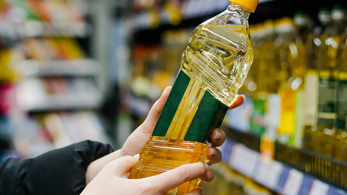 Woman choosing sunflower oil in the supermarket. Close up of hand holding bottle of oil at store.