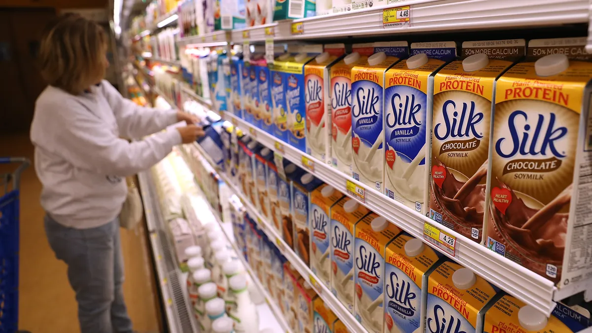 Containers of Silk soy mik are displayed on a grocery store shelf. A woman is seen looking at the display.