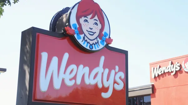 A photograph of a red sign with white lettering that says Wendy's. Above the sign is a log of a girl with red hair and freckles.