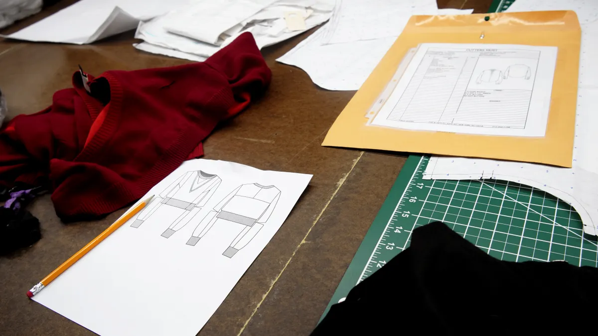 Garments lie on a table alongside pattern designs and other sewing items.