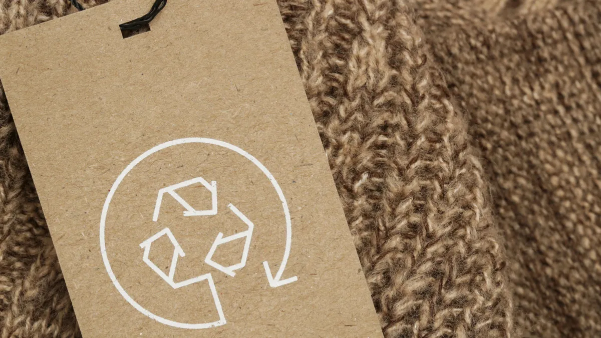 A brown recycling tage lies on top of a brown knit fabric.