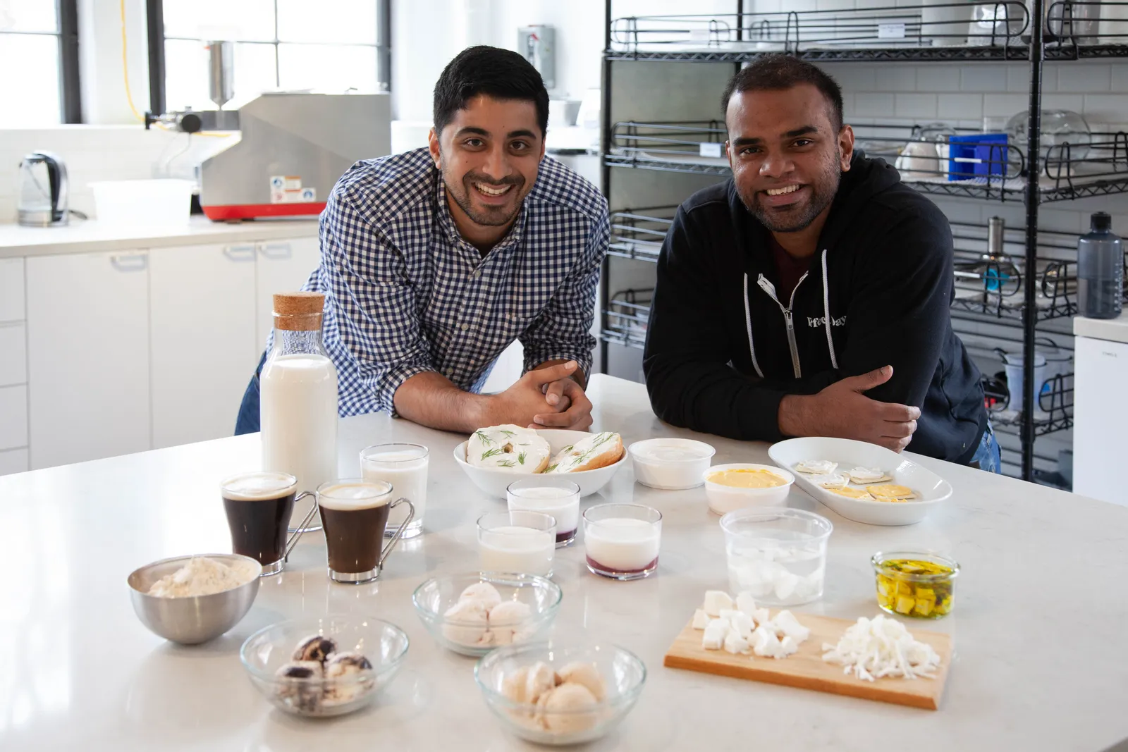 Two people pose for a portrait in front of a variety of milk products in a kitchen lab.