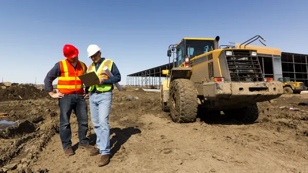 Two construction workers look at a clipboard on a jobsite.