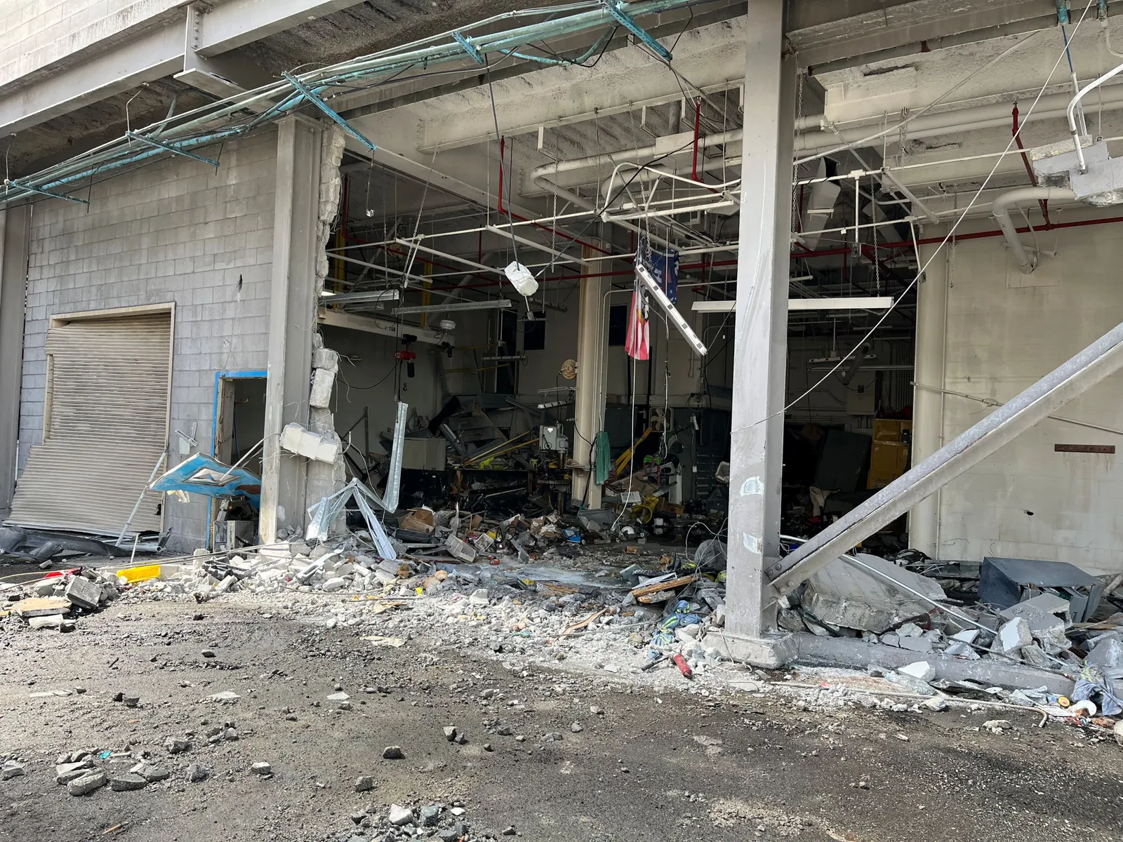 Debris is seen in an industrial yard where a cinder block wall has been partially removed from an adjacent building.