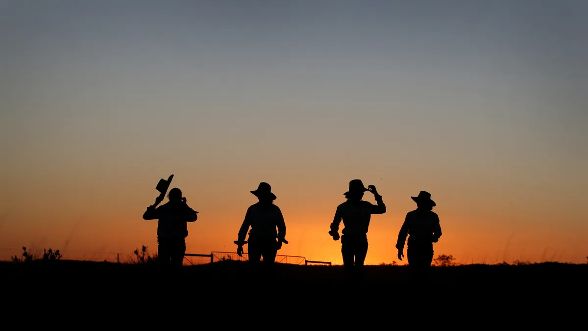 Silhouettes of ranchers are seen on the horizon