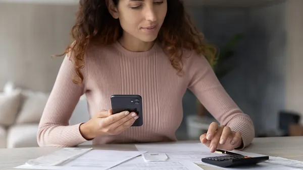 Person sit at desk calculating numbers on calculator with papers and phone.