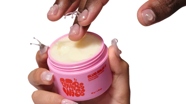 Three hands holding three bright pink and red skincare bottles