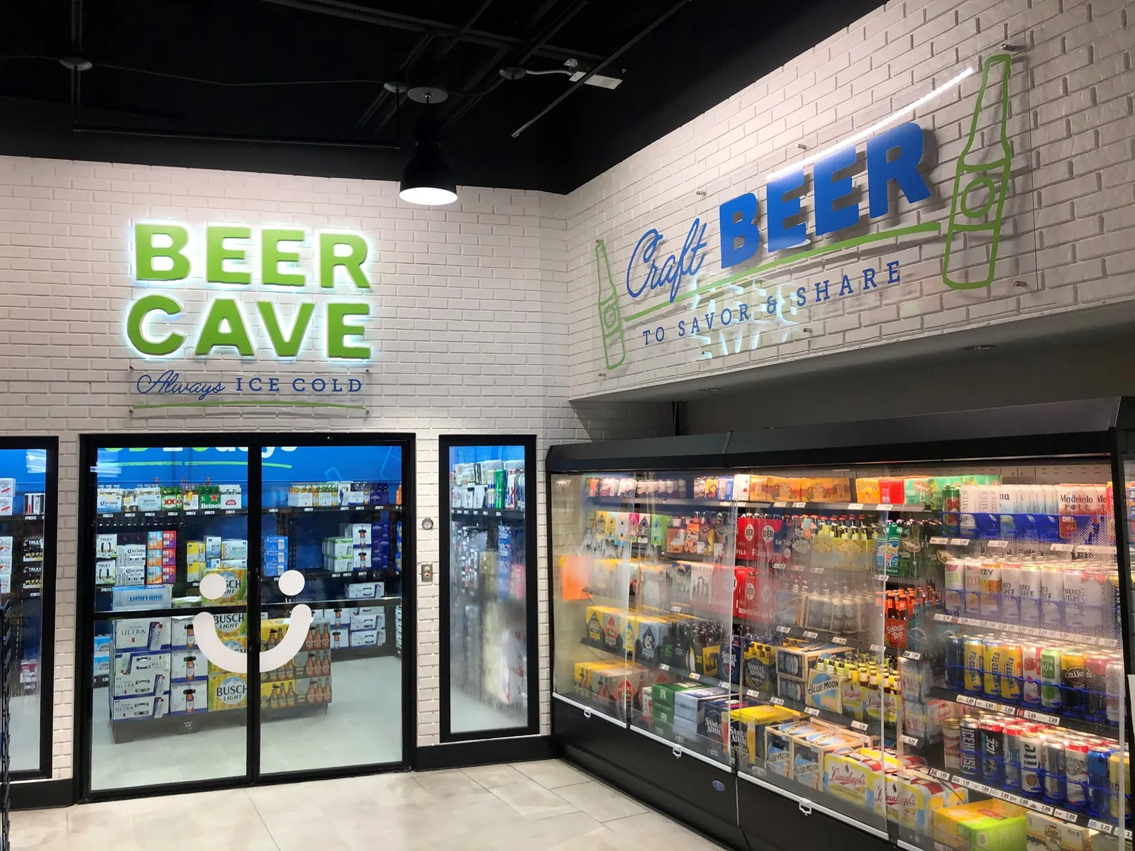 A photo of a beer cave and beverage cooler. Signs on the wall read &quot;read cave always ice cold&quot; and &quot;craft beer to savor and share.&quot;