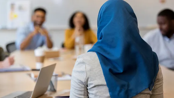 A hijabi worker sits with her back turned to the camera