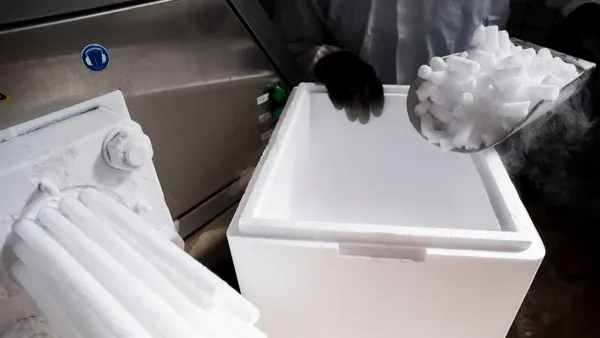 Dry ice is being made from a machine while a person's hands wearing protective gear scoops the dry ice pellets.