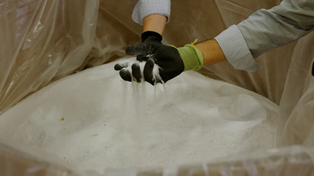 A hand in a black glove picking up a white powdery substance as it flows out of the person's hand.