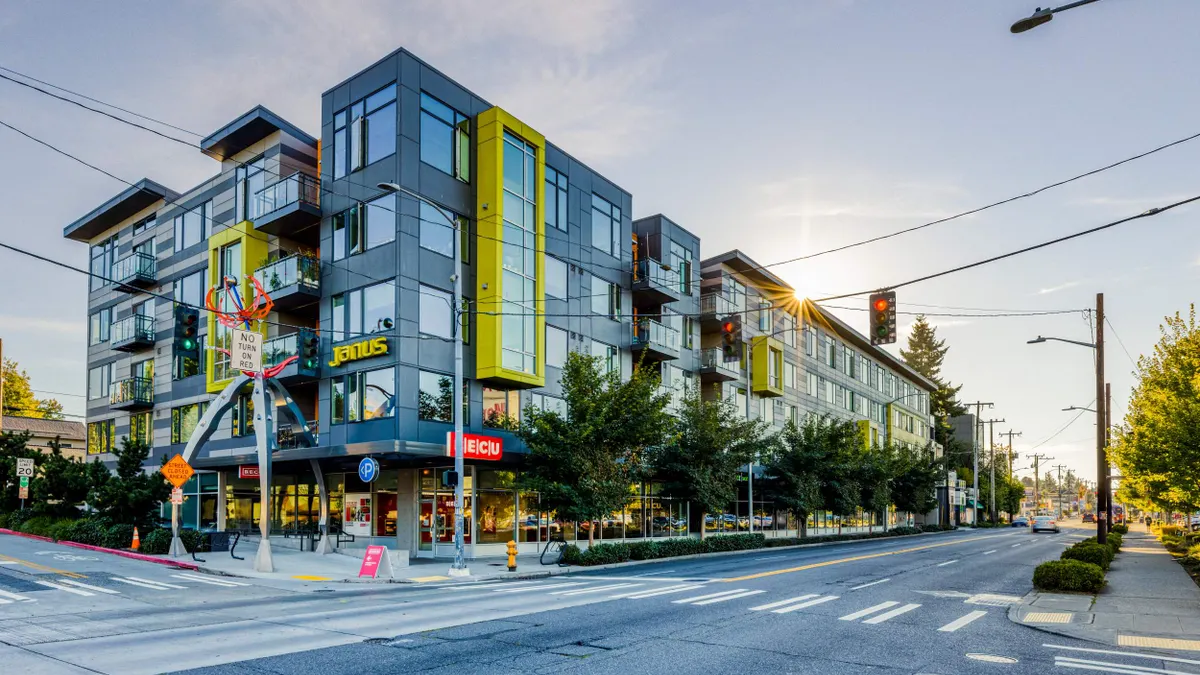 Grey and yellow, five-story apartments with ground floor retail on street corner.