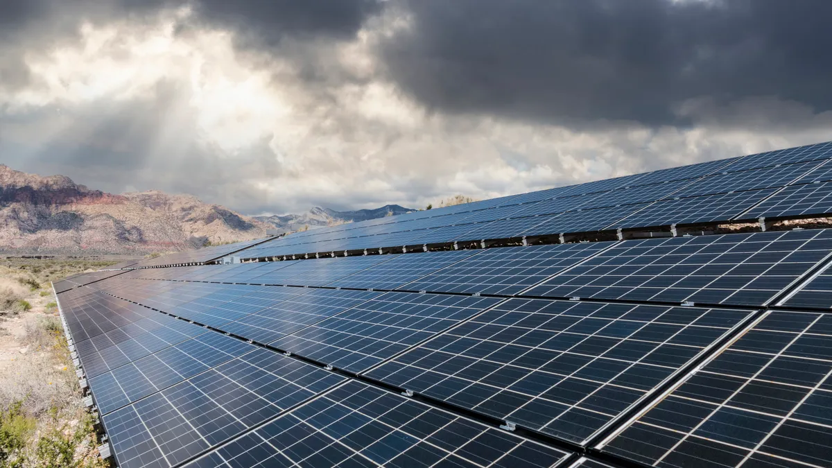 Solar panels in a desert with storm clouds in the background.