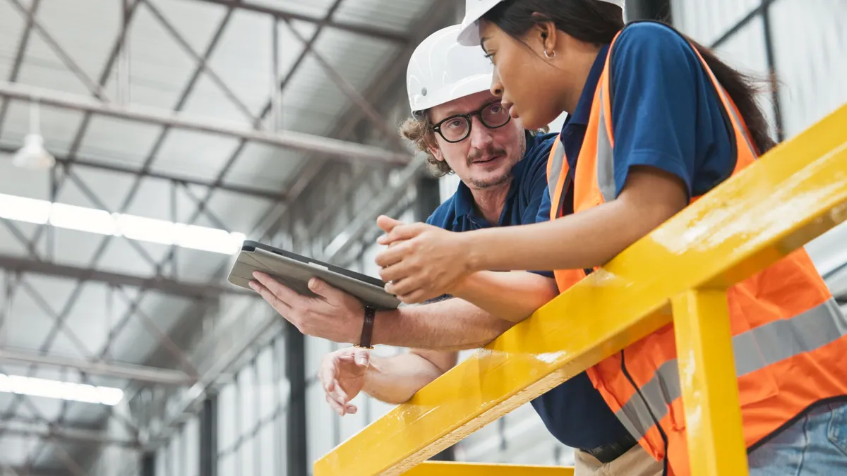 Two construction workers chat on a jobsite while holding a tablet.