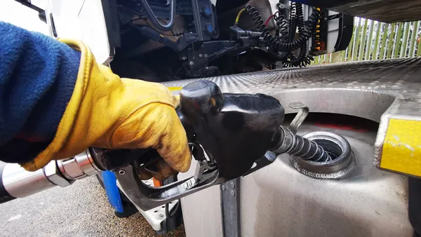 A driver wearing a yellow glove fuels a heavy-duty truck with diesel at a pump.