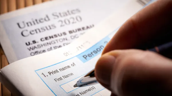 A person's hand with a pen filling out a form that says "United States Census 2020" and "United States Census Bureau."