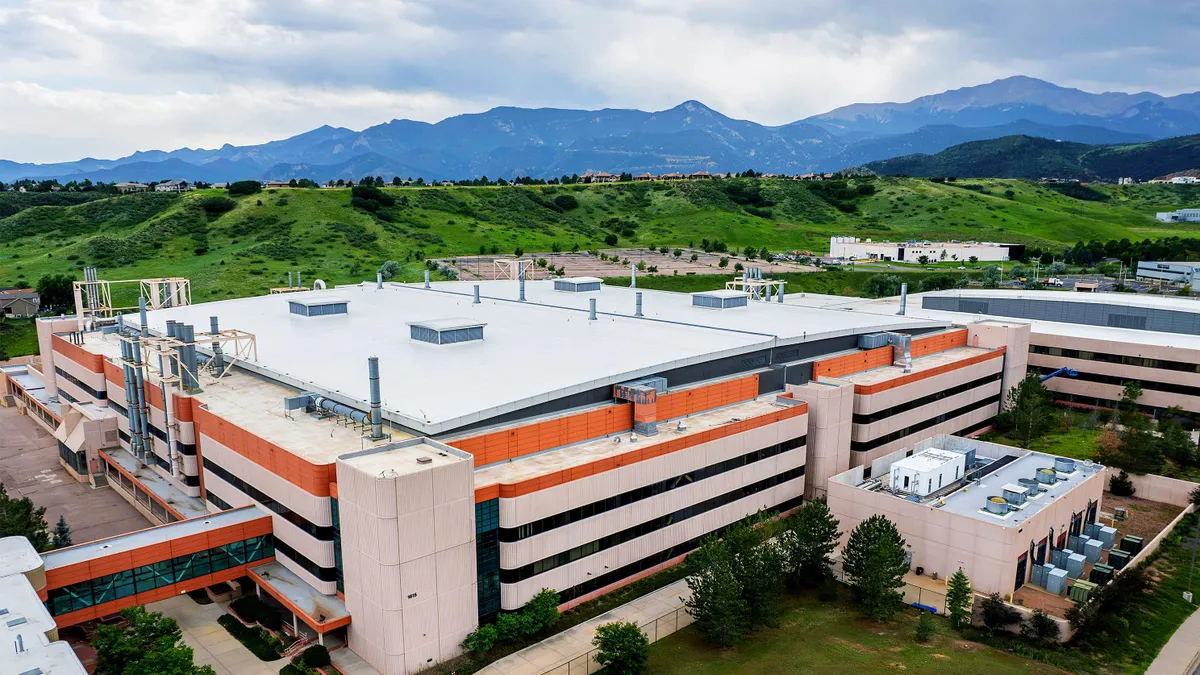 A beige, orange and white building surrounded by green landscape and mountains.