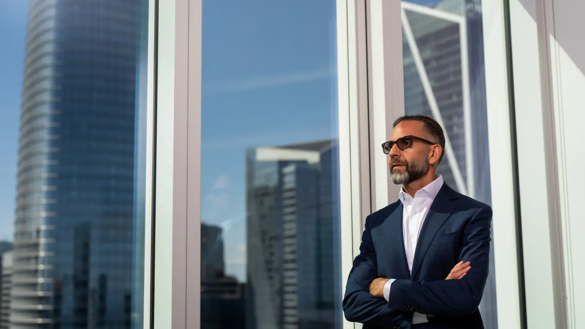 A man in a suit looks out of a window in a tall building.