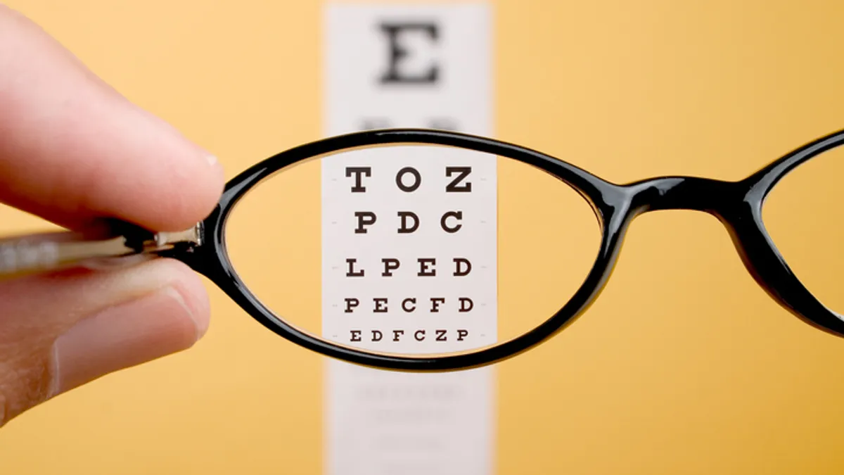 Letters appear clearer in an eye chart on a yellow wall viewed through glasses.