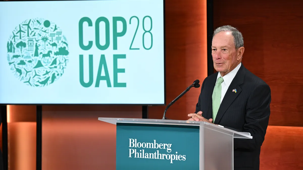 A person stands at a podium that reads "Bloomberg Philanthropies." A sign behind the person reads "COP28 UAE".