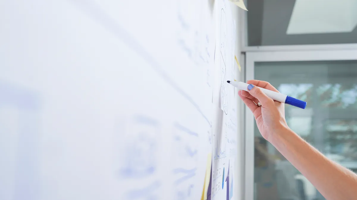 Hand of female business executive drawing diagram on office whiteboard with blue marker.