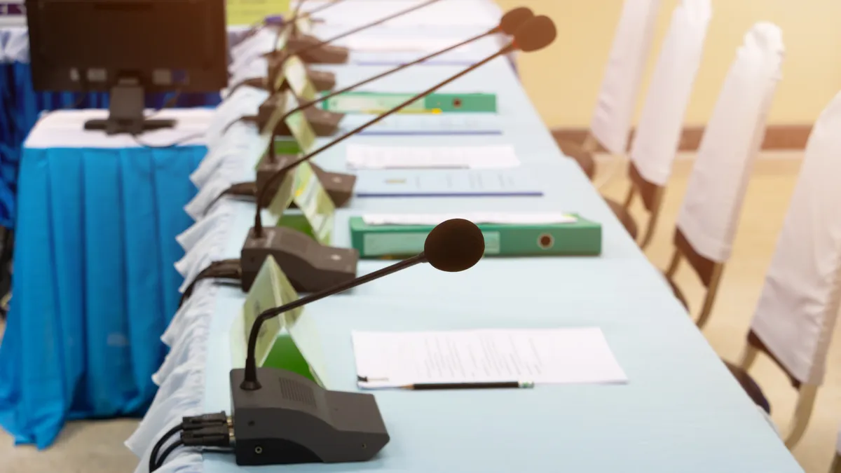 Microphones and binders sit on a long table.