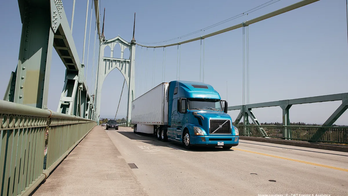 A car and a truck drive along a bridge.