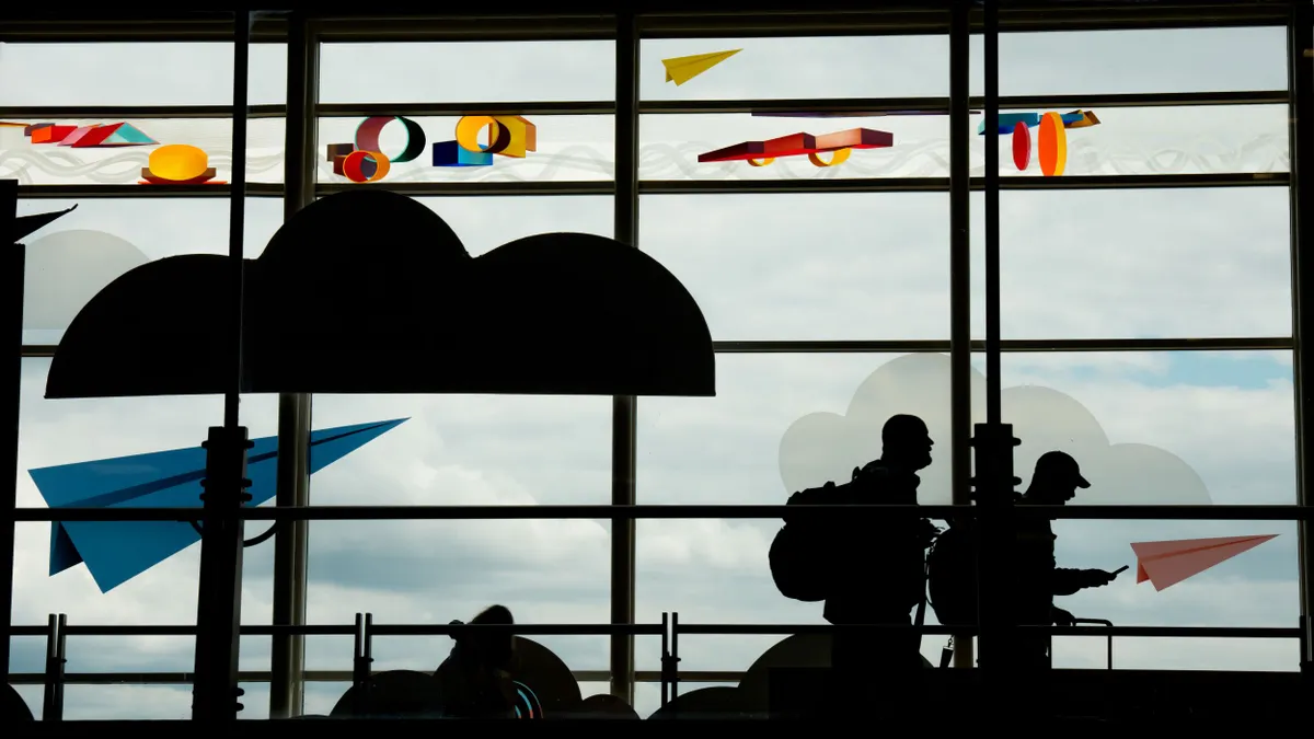 Two passengers walk through an airport as one looks at a phone.