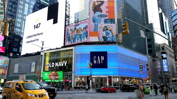 Pedestrians and cars pass by at intersection in front of Old Navy and Gap storefronts.