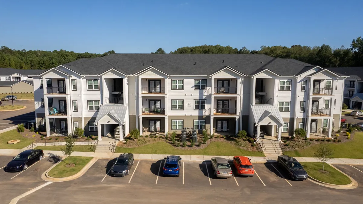 Three-story apartments with parking lots and cars in the foreground.