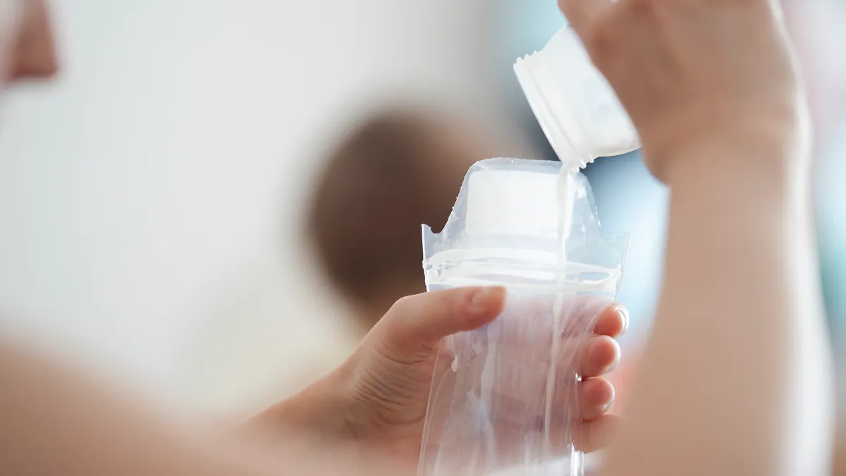 Someone pours breastmilk from a bottle into a storage bag.