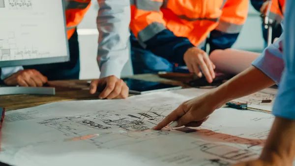 A shot of a table as several people in construction gear stand around in a meeting.