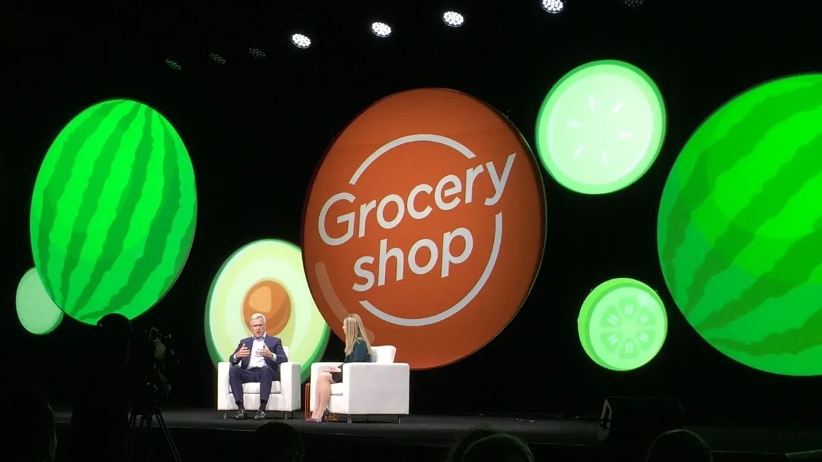 Two people sitting in white chairs in front of circular signs on a stage