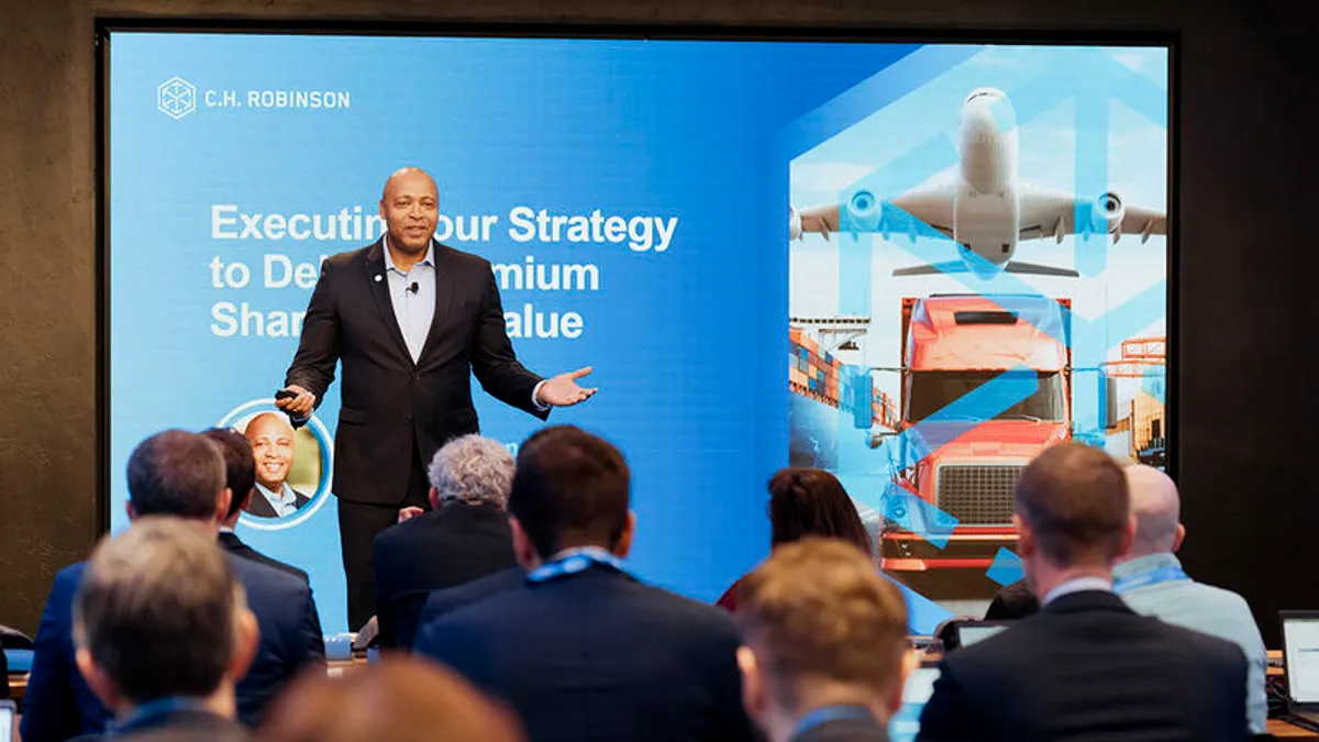 A crowd sits in chairs in front of tables and computers while listening to C.H. Robinson President and CEO Dave Bozeman present for a company investment event.