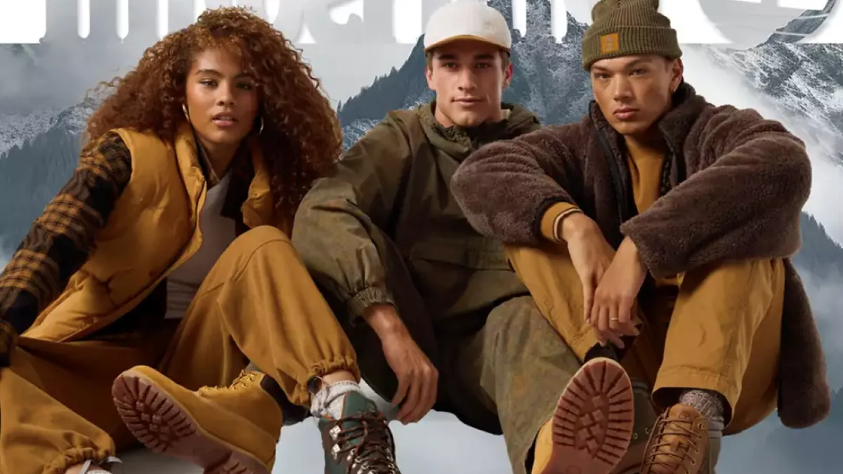 Three people sit on the floor looking at the camera and wearing brown outerwear.